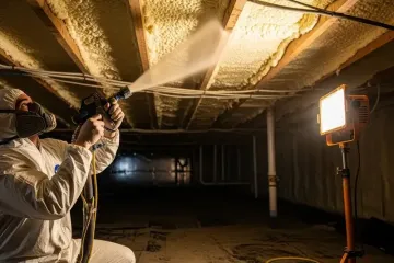 Applying airtight spray foam insulation in crawl space of family home to prevent heat loss during cold seasons in energy retrofit process.